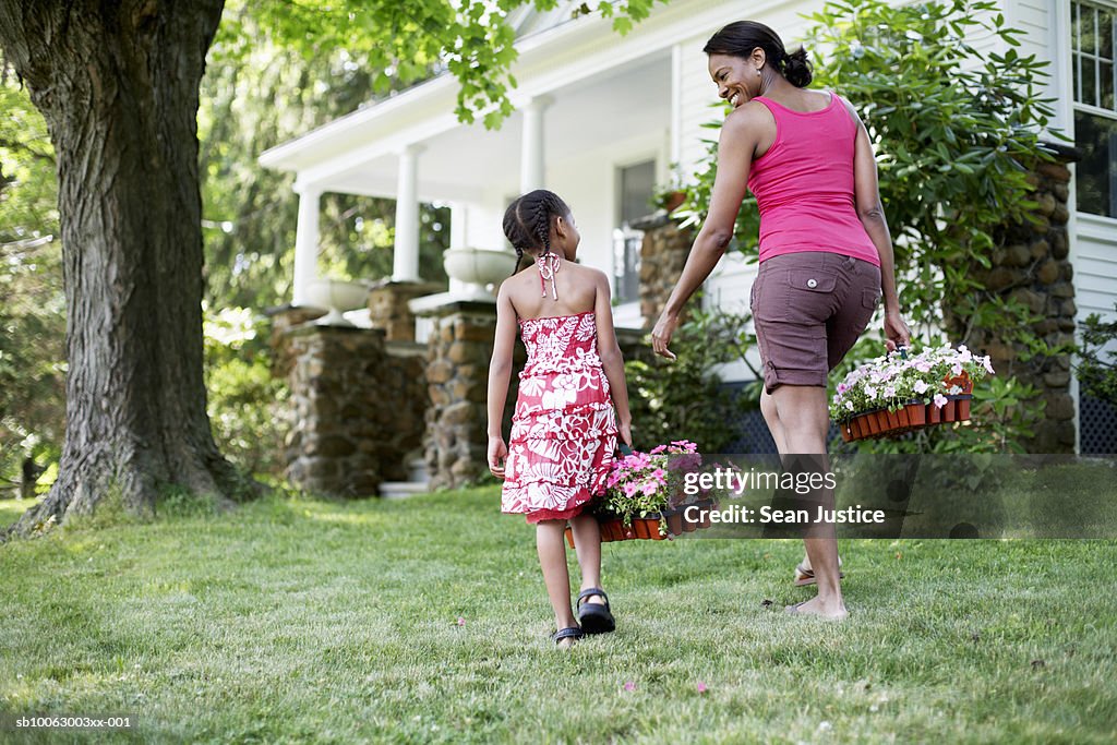 Mother and daughter (8-9 years) in garden outside house, carrying flowers, rear view