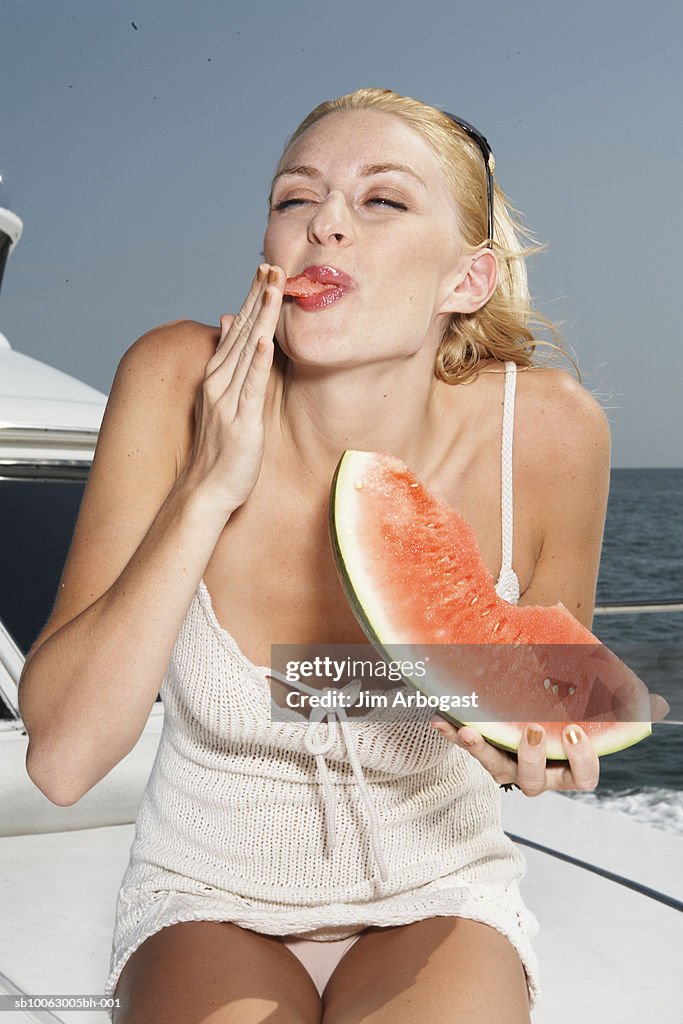 Young woman eating slice of watermelon on boat, licking finger