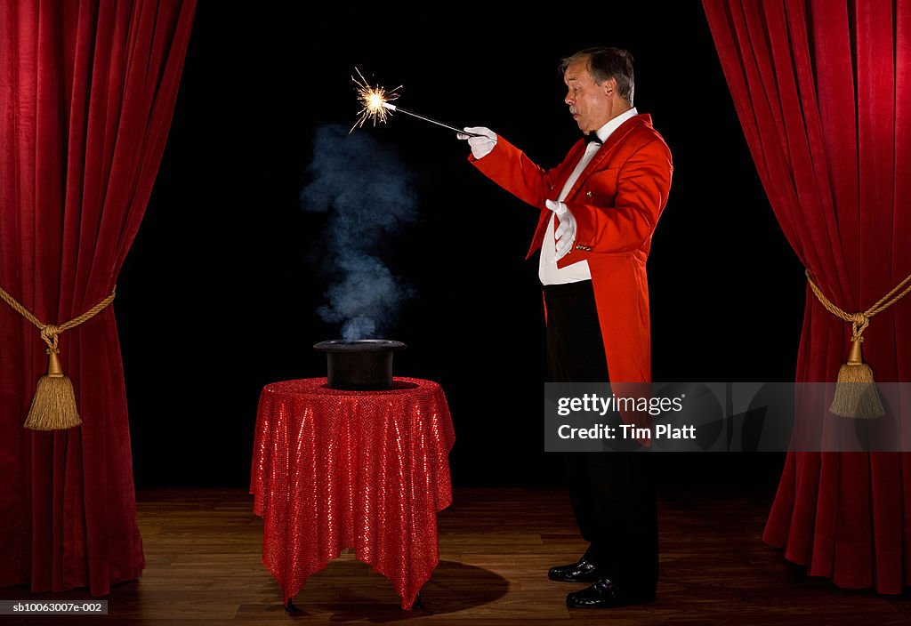 Magician with smoke in hat on stage, side view