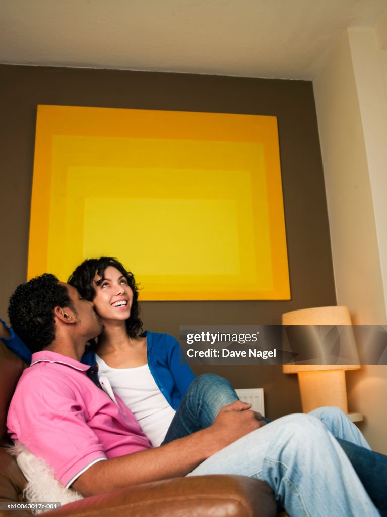 Young couple sitting in armchair with large yellow image on wall