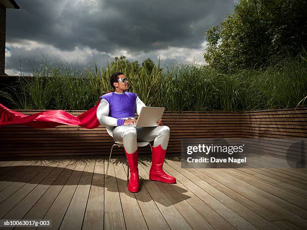 young man dressed as superhero, sitting outdoors and using laptop - ominous computer stock pictures, royalty-free photos & images