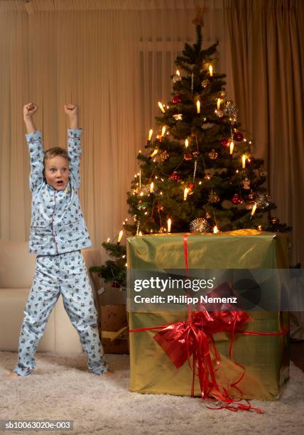 boy (6-7) standing with arms up besides christmas tree - drapeado stock pictures, royalty-free photos & images