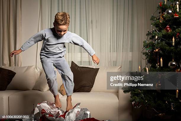 boy (6-7) jumping on wrapping paper by christmas tree - nightdress stock pictures, royalty-free photos & images