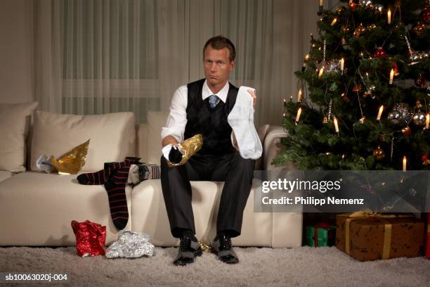 man sitting on sofa holding sock, portrait - bad christmas stock pictures, royalty-free photos & images