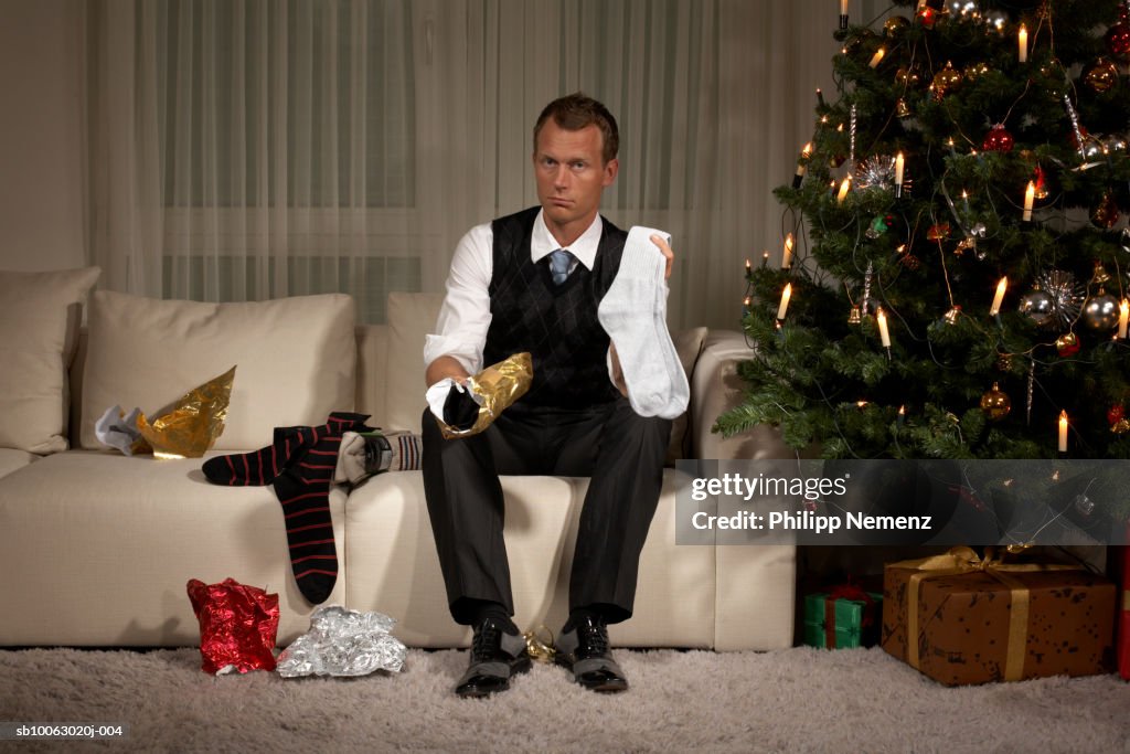 Man sitting on sofa holding sock, portrait