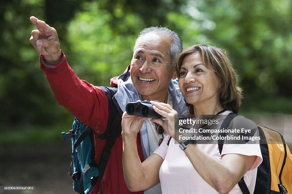 Senior couple hiking, woman holding binoculars, man pointing upwards