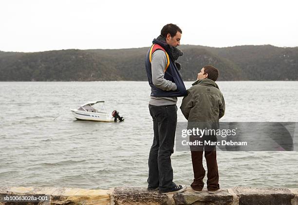 father and son (10-11) standing on wall at edge of lake, rear view - buitenboordmotor stockfoto's en -beelden
