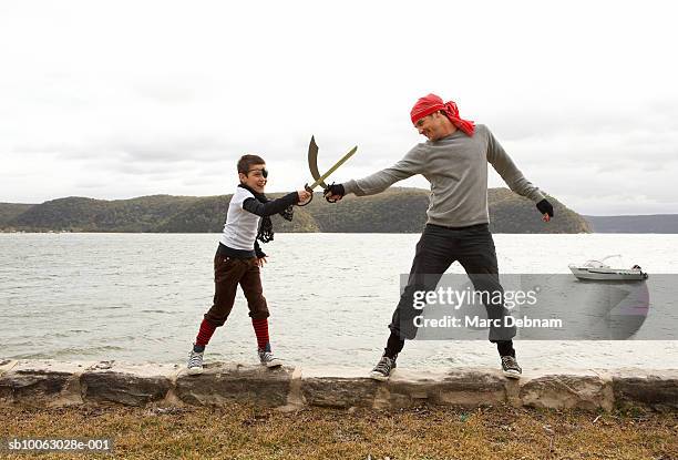 boy (10-11) and father dressed as pirates, mock-duelling, on wall at edge of lake, side view - pirate kids ストックフォトと画像