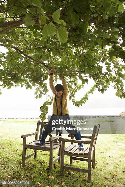 boy (10-11) hanging from tree branch, standing on outdoor chairs, in yard - hanging in garden bildbanksfoton och bilder