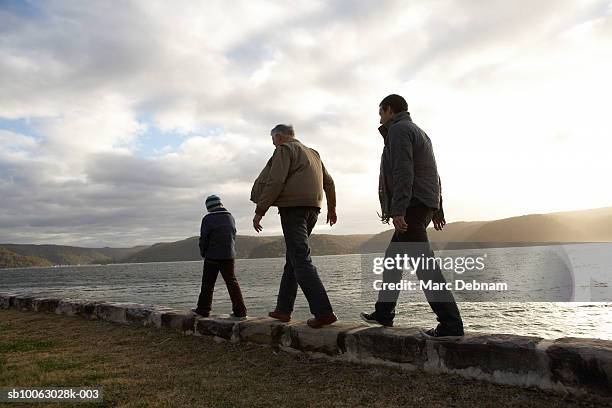 boy (10-11), grandfather and father walking on wall at edge of lake, rear view - grandpa son stock pictures, royalty-free photos & images