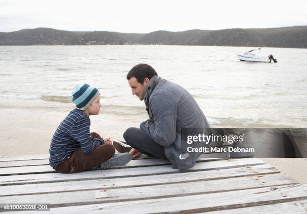 father and son (10-11) sitting at end of dock at edge of lake, talking, side view - boat side view stock pictures, royalty-free photos & images