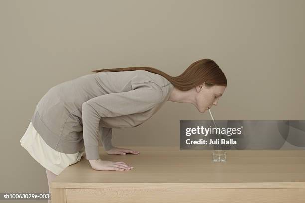 young woman leaning on table drinking water with straw, side view - strohhalm stock-fotos und bilder