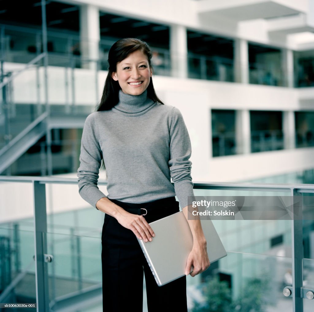 Young businesswoman holding laptop, smiling, portrait