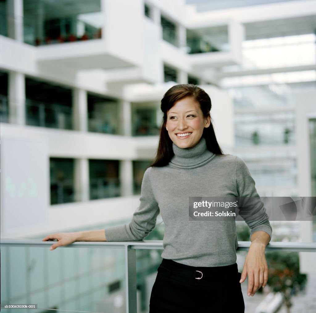 Businesswoman leaning on railing, looking away, smiling
