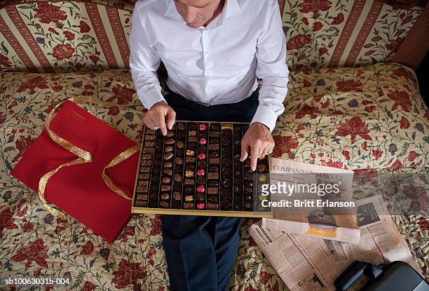 businessman sitting on hotel bed with box of chocolates - newspaper luxury stock-fotos und bilder