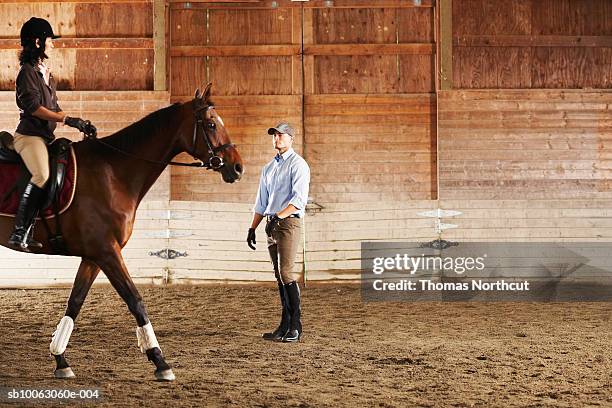 young man standing next to rider and her horse in a training stable - learning stock pictures, royalty-free photos & images
