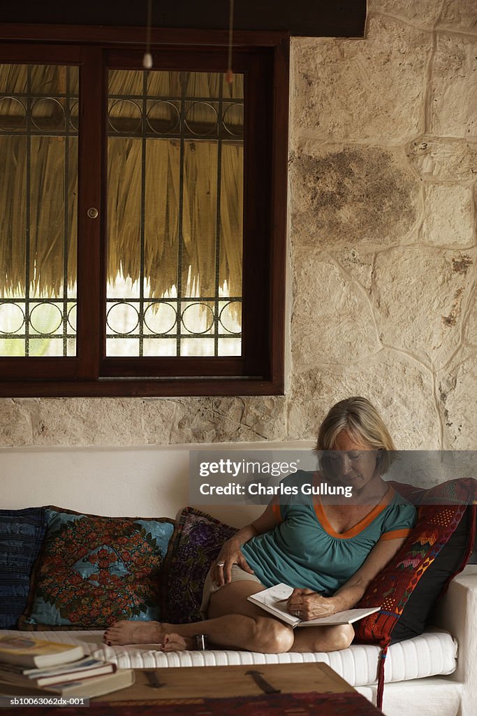 Mature woman sitting on sofa, writing in book