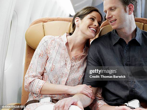 mid adult couple cuddling on airplane - couple airplane stockfoto's en -beelden