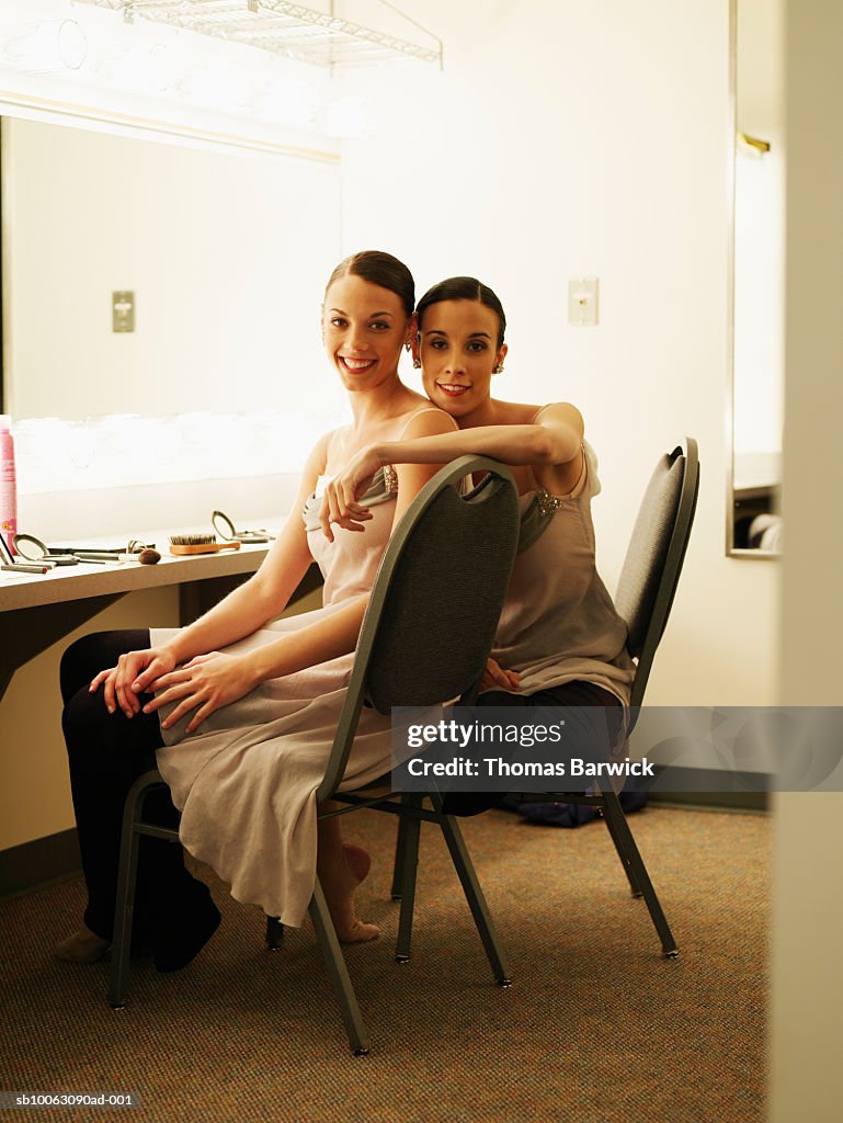 Two ballerinas in costume sitting in dressing room, smiling, portrait