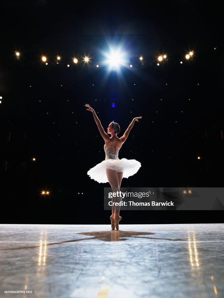Prima ballerina en pointe on stage, arms raised, rear view