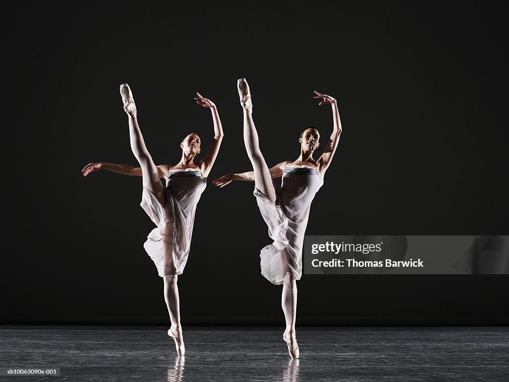 Two ballerinas dancing on stage, legs raised