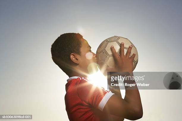 profile of boy (12-13) kissing football, lens flare - fußball emotional stock-fotos und bilder