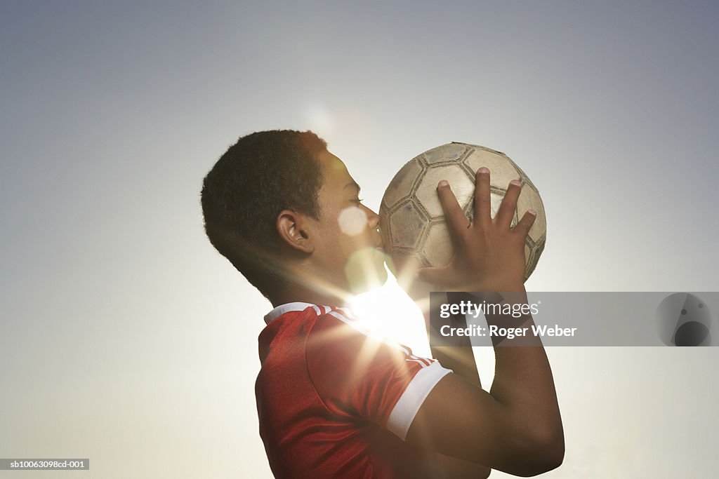 Profile of boy (12-13) kissing football, lens flare