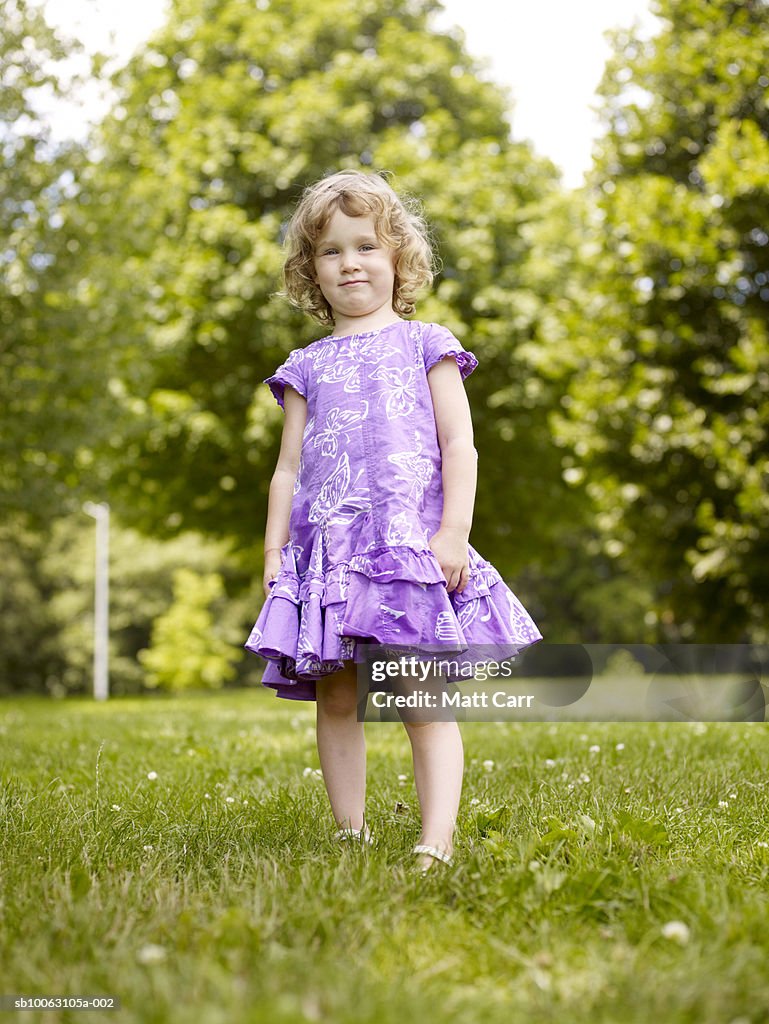 Girl (4-5) standing in park, smiling, low angle view