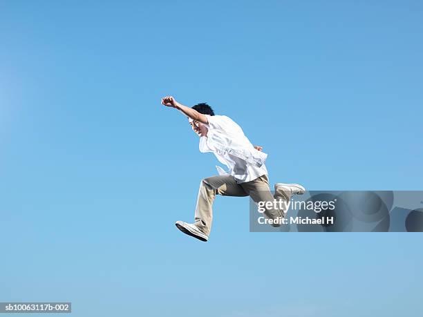 young man leaping in blue sky - action hero ストックフォトと画像