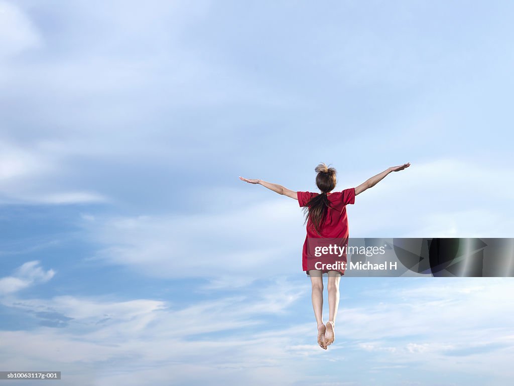 Young woman leaping in sky, arms outstretched, rear view