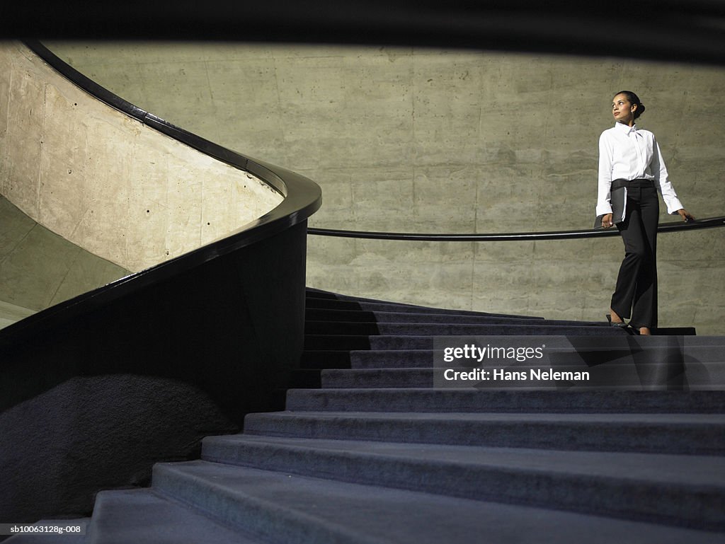 Business woman walking down stairs in office, low angle view