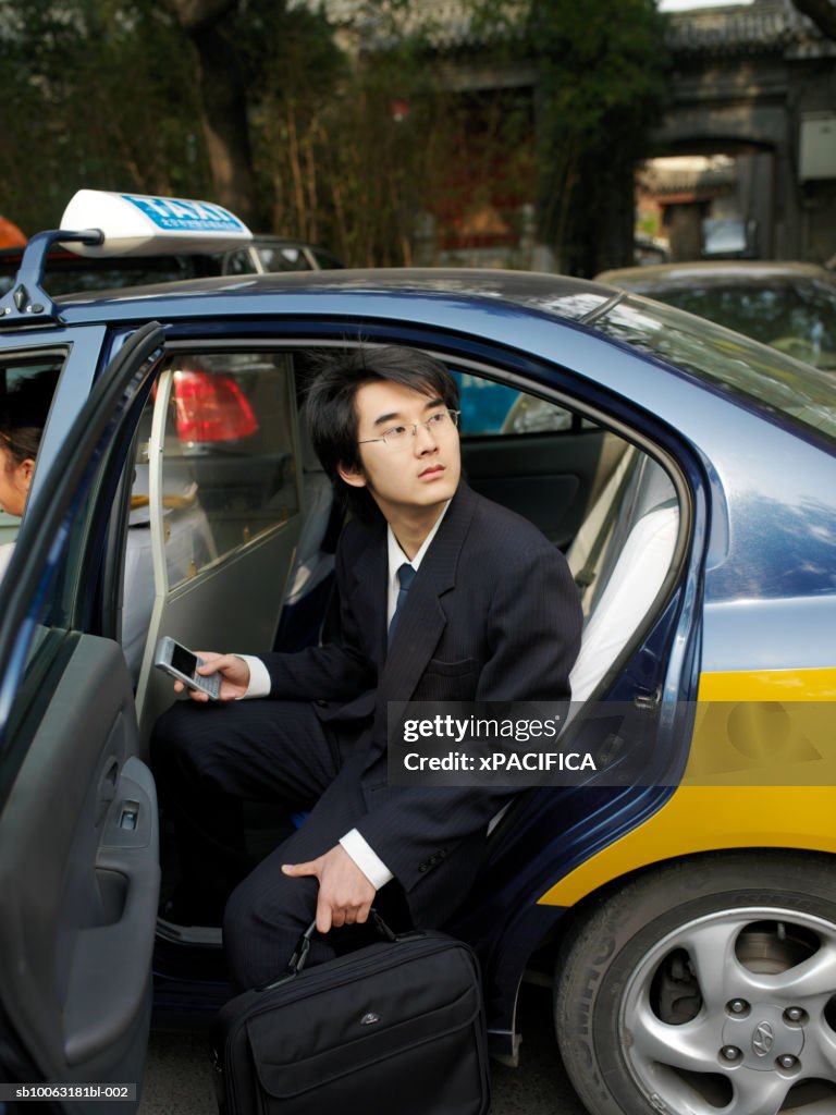 China, Beijing, young business man in taxi, holding briefcase and phone, looking up