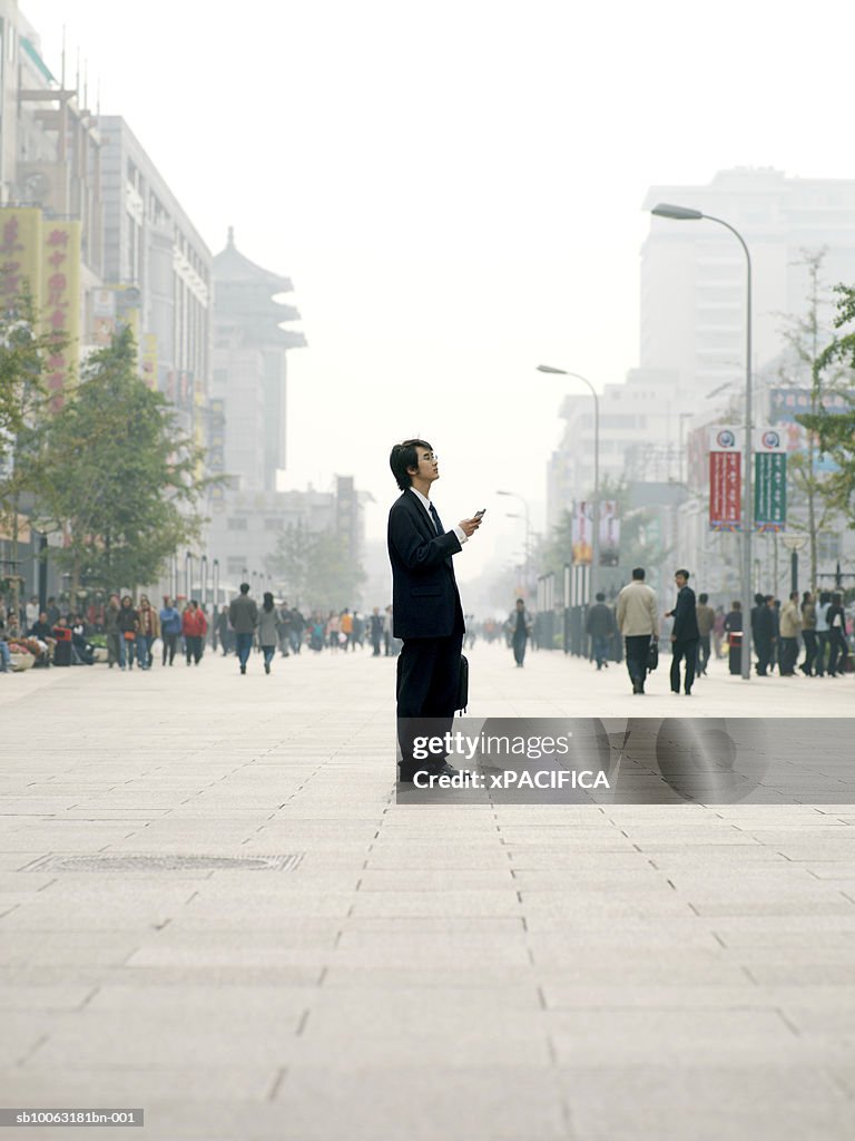 China, Beijing, business man standing in square, holding mobile phone