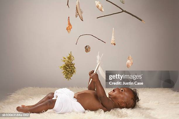 baby boy (8 months) lying on furry carpet, objects suspended above (digital composite) - kids in diapers - fotografias e filmes do acervo