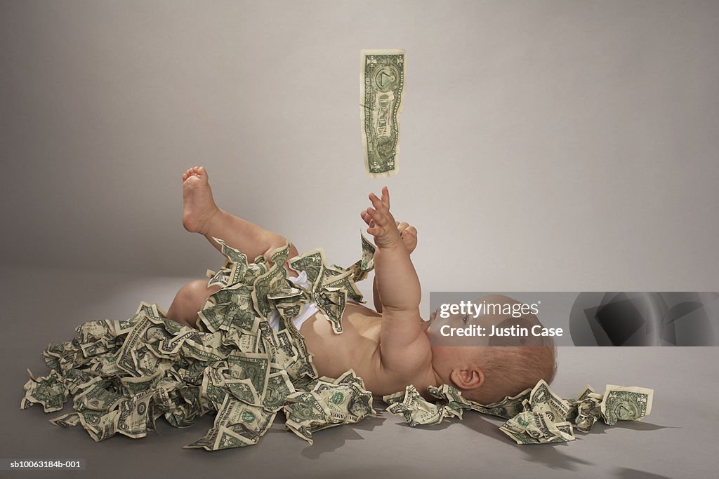 Baby girl (5 months) lying down covered with us dollar bills falling from above