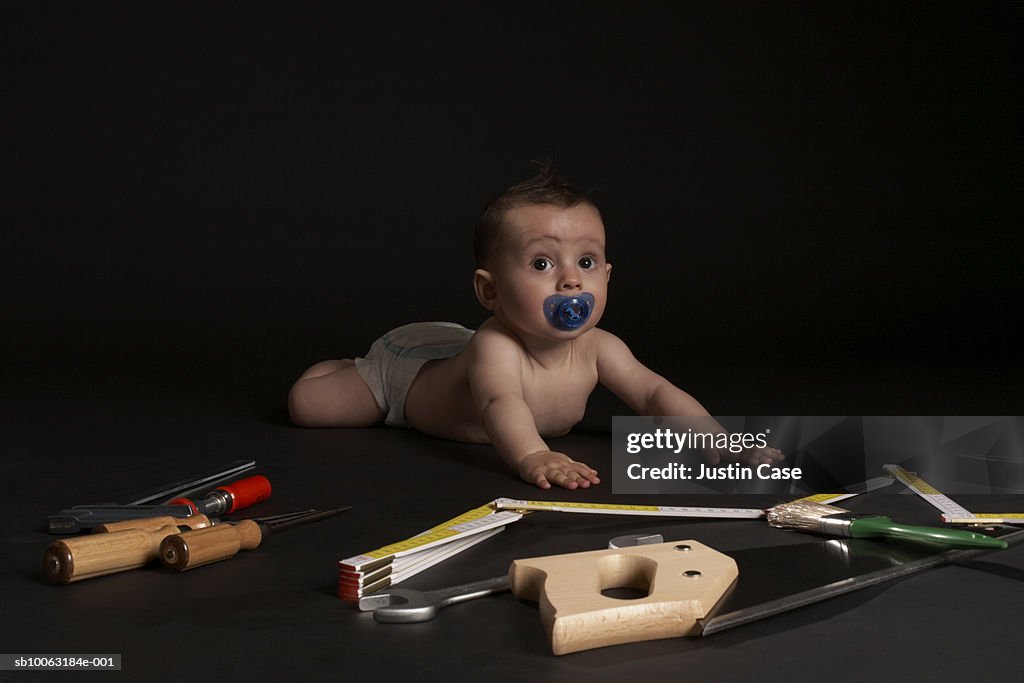 Baby boy (5 months) lying on belly surrounded with tools