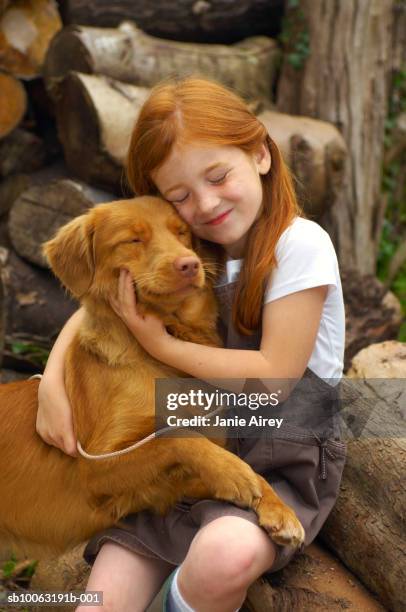 girl (6-7) with eyes closed, embracing dog on wood pile - dog eyes closed stock pictures, royalty-free photos & images