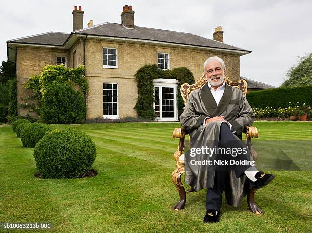 senior man sitting on antique chair in garden, smiling. looking at camera - rich stockfoto's en -beelden