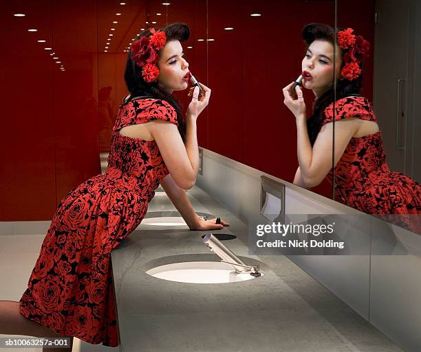 young woman applying lipstick in mirror of public lavatory, side view - nightclub bathroom stockfoto's en -beelden