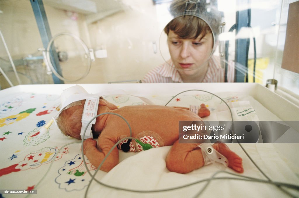 Woman looking at new-born baby (0-3 months) in incubator