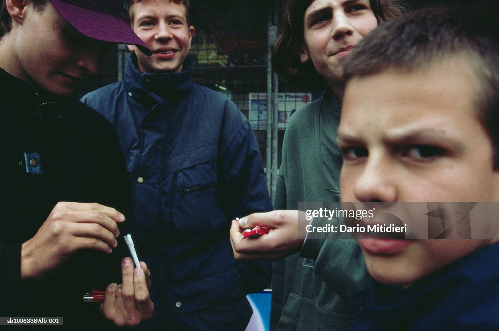 Group of teenage boys (13-15) rolling joint in street