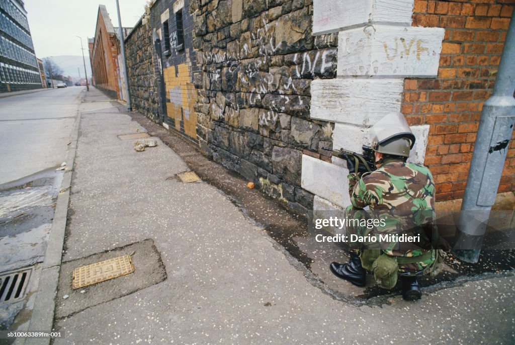 Northern Ireland, Belfast, British soldier crouches with gun on street corner