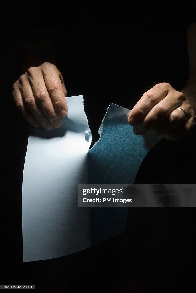 Man tearing piece of paper, close-up on hands, studio shot