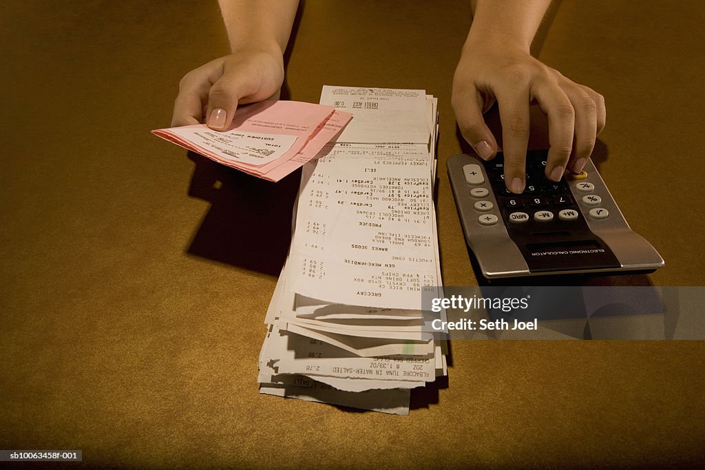 Woman calculating receipts on floor, view of hands, elevated view