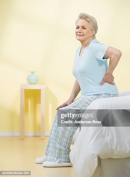 senior woman sitting at edge of bed with hand on back, portrait - back pain bed stock pictures, royalty-free photos & images
