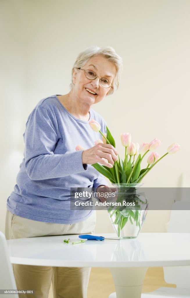 Senior woman arranging flowers in vase at home, portrait