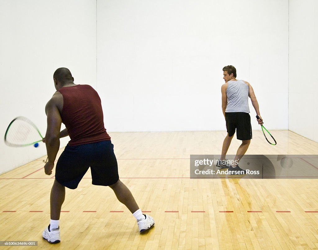 Two men playing racquetball indoors, rear view