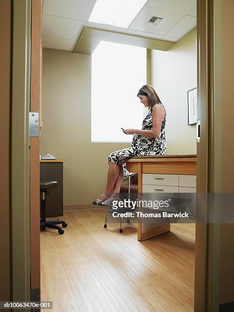 pregnant woman sitting on table in examination room, using mobile phone - examining table stock pictures, royalty-free photos & images