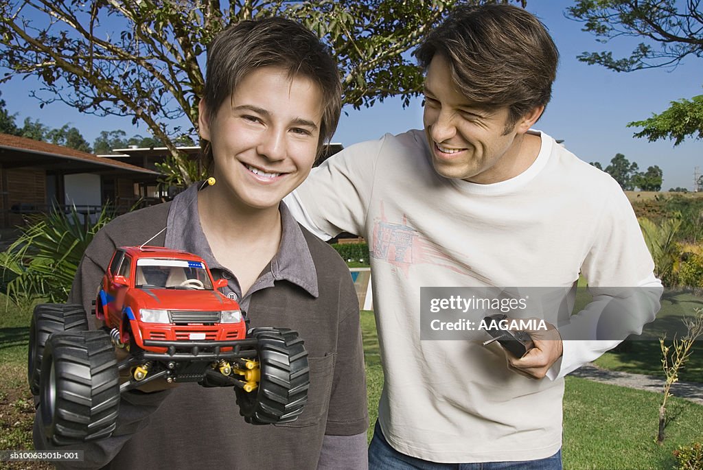 Father and son (13-14) playing with RC car at garden, smiling