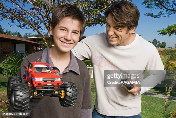 father and son (13-14) playing with rc car at garden, smiling - car remote toy stock pictures, royalty-free photos & images